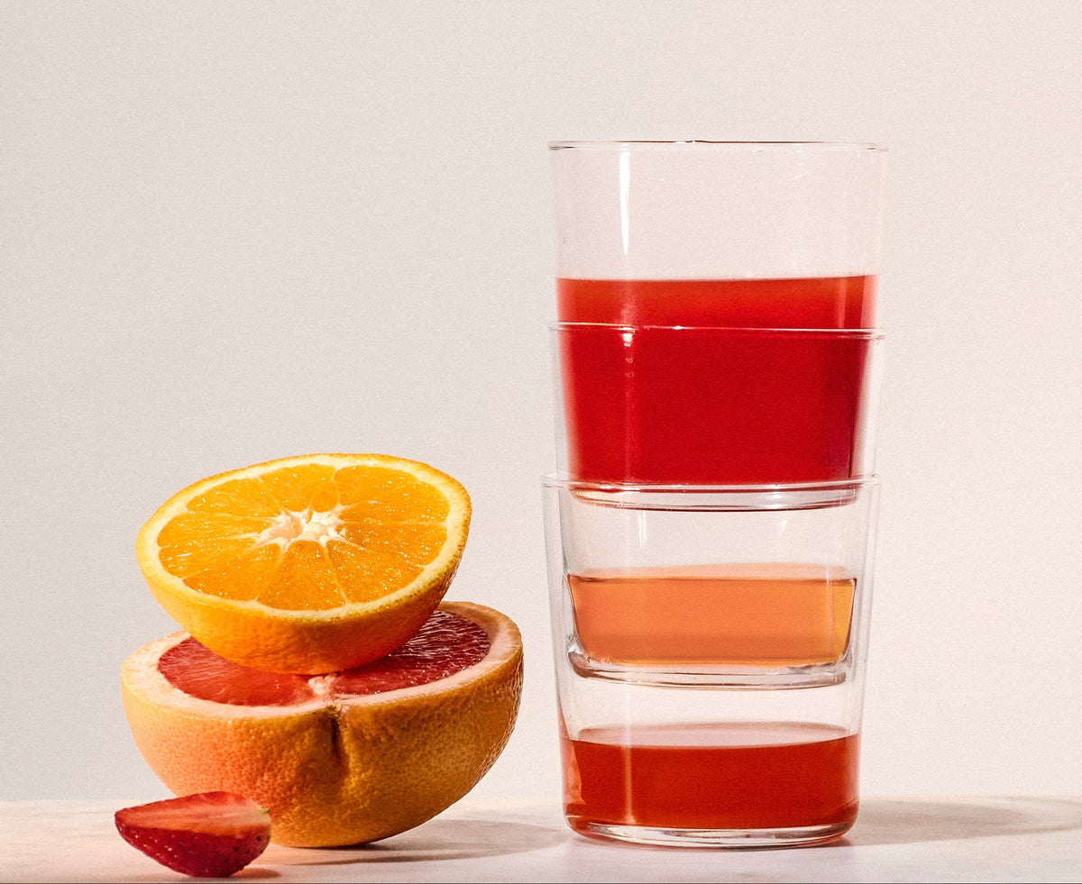 Tre glass med ferdige drikker stablet oppå hverandre ved siden av en appelsin, en grapefrukt og et jordbær