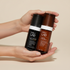 Two skincare bottles from INDA+ LAB on a white background. The left bottle is a black Daily Defence Cream SPF 30 bottle with a black cap, and the right bottle is an amber-brown Firming Face Cream bottle with a dark brown cap.