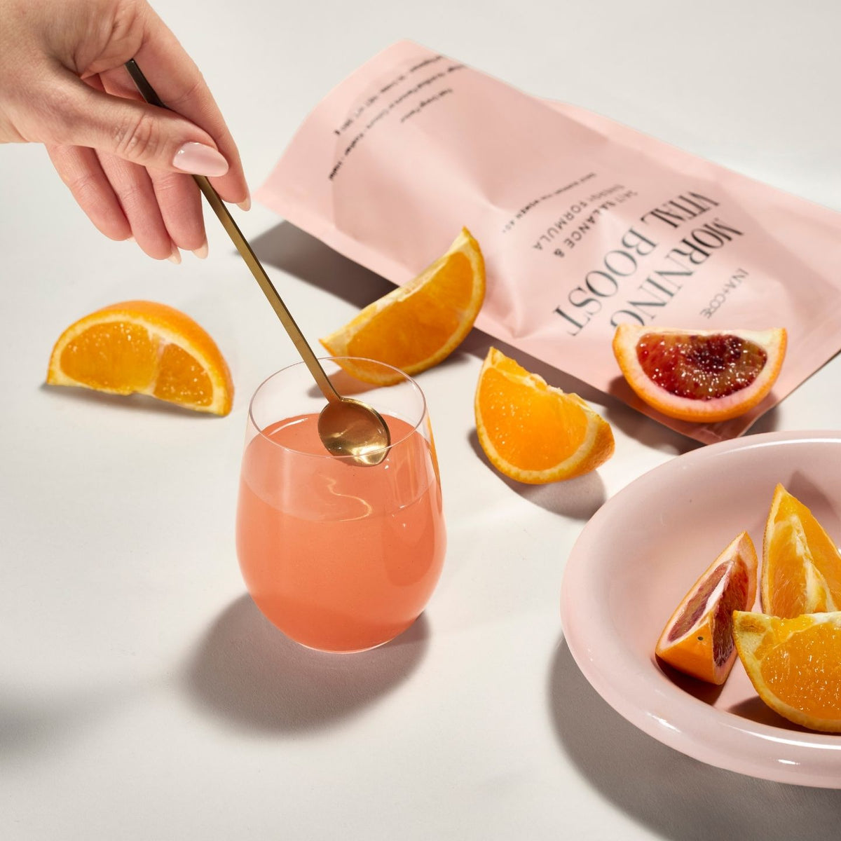 Et glass Morning Vital Boost med appelsinbåter og posen i bakgrunnen